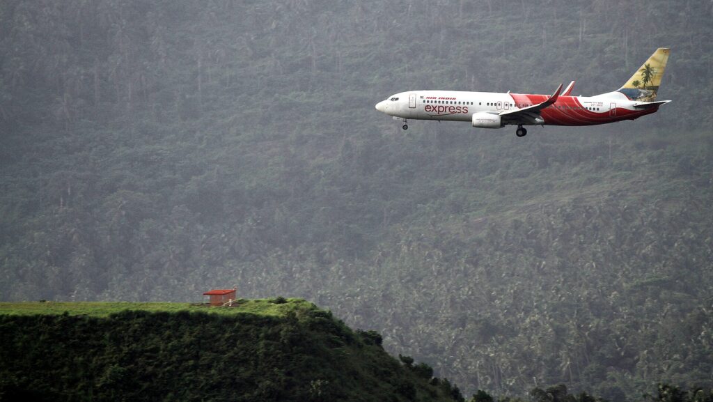 An Air India Express Boeing 737-800 on approach over green hills to the tabletop runway at Calicut airport