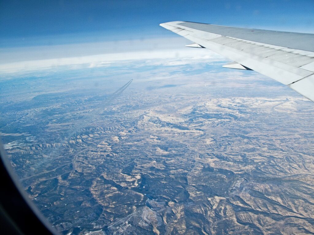 View from an airliner window at cruise altitude showing another aircraft and its contrail crossing below