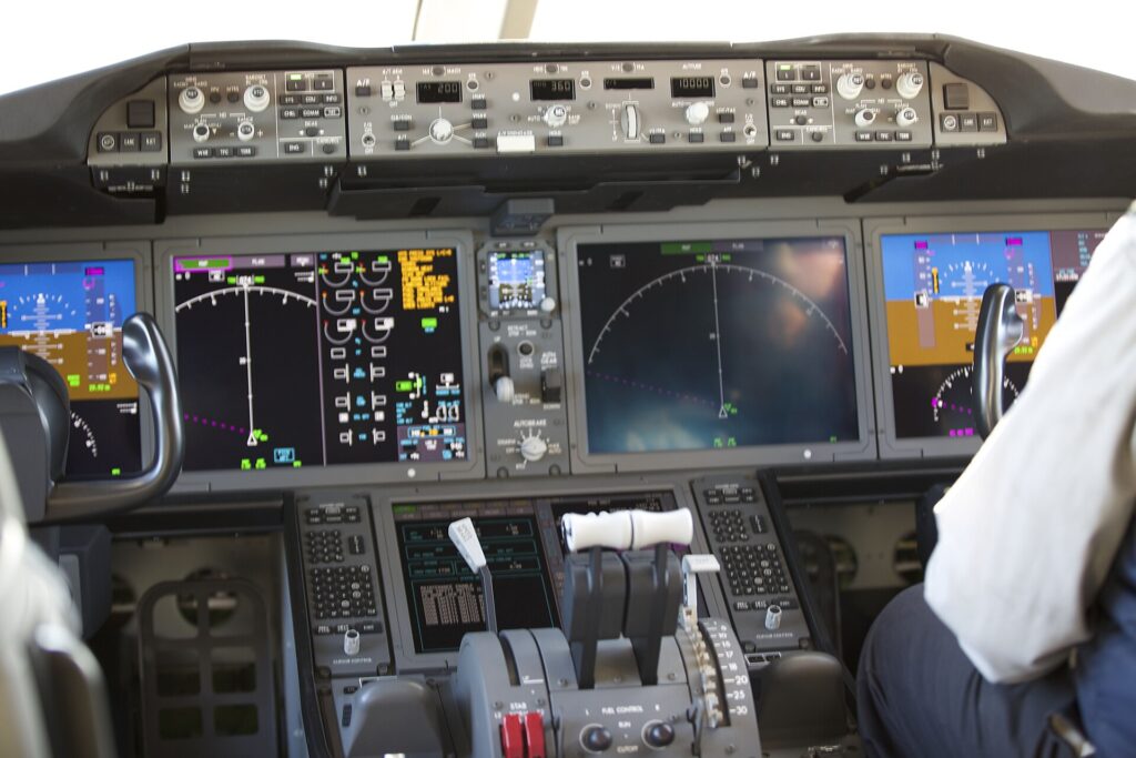 Boeing 787 flight deck with large displays and a pilot in the right-hand seat