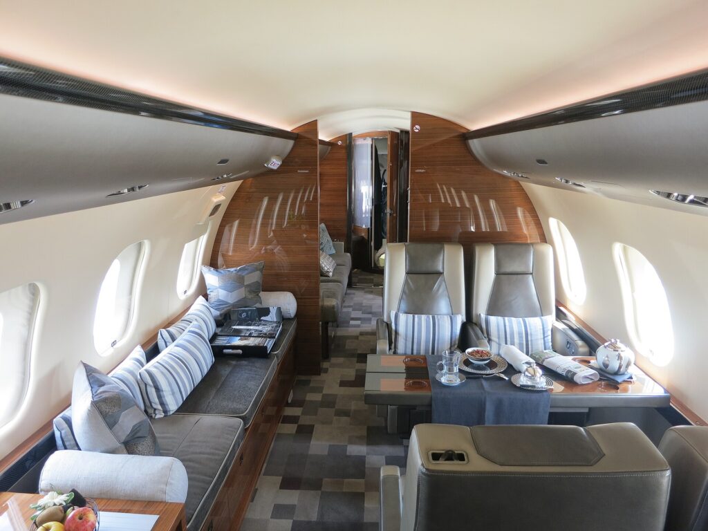 Wide cabin of a Bombardier Global 6000 with a long divan sofa, leather club seats and wood cabinets