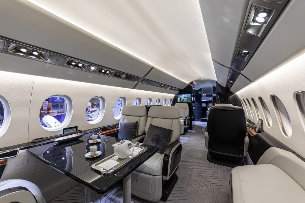 Falcon 6X cabin mock-up with cream leather seats, a dining table and large windows
