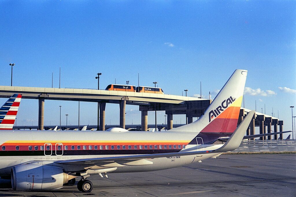 An American Airlines Boeing 737 in AirCal heritage colors parked under the Skylink train track at Dallas Fort Worth airport