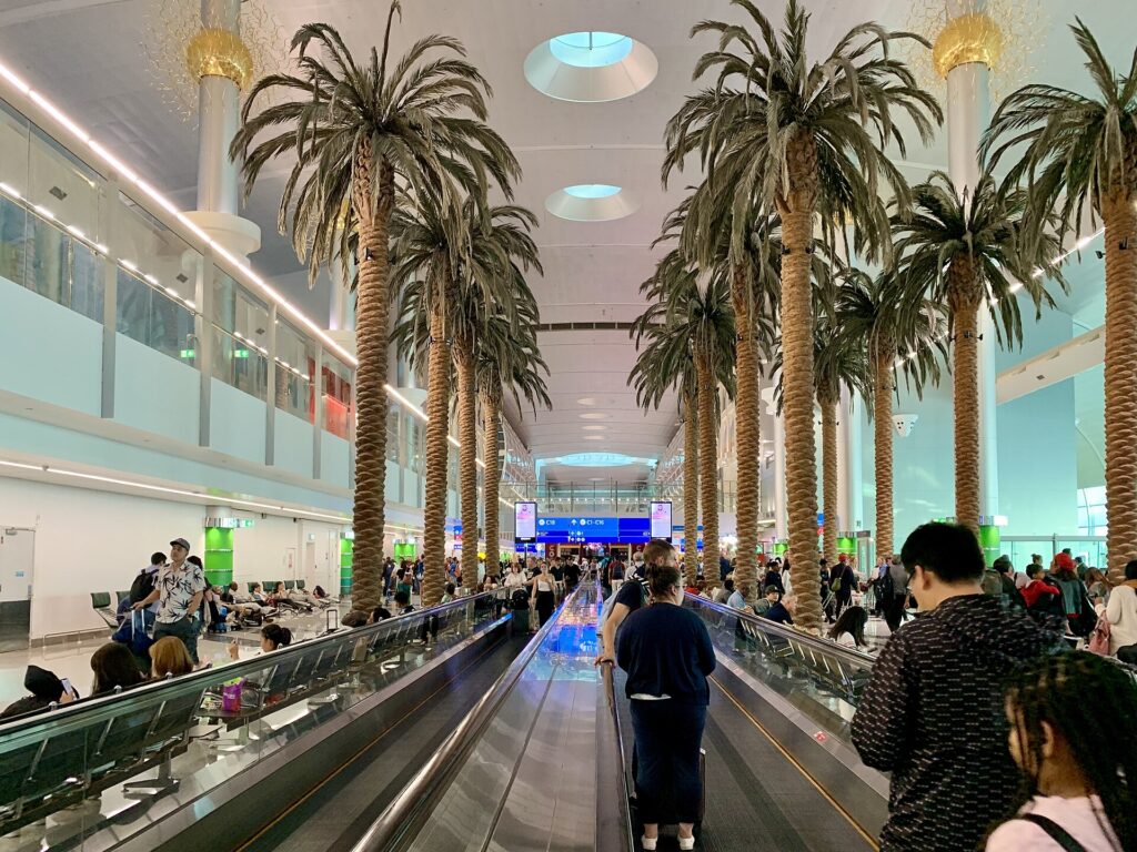 Passengers on a moving walkway under rows of palm trees inside Dubai International Airport Terminal 3