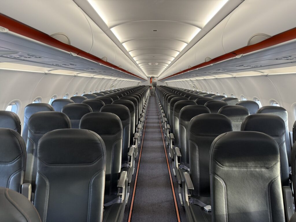 The empty cabin of an easyJet Airbus A320neo, with rows of dark grey leather seats either side of the aisle and orange trim on the overhead bins