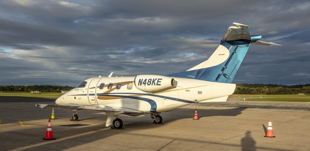 White and blue Embraer Phenom 100EV N48KE parked with its door open at sunset