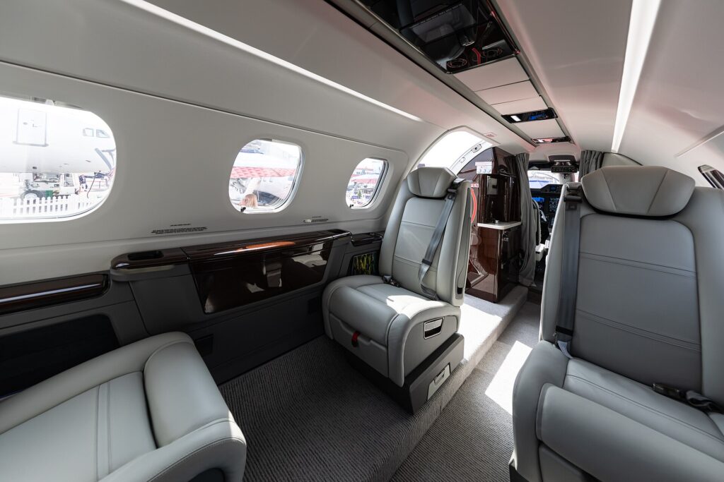 Wide-angle view of a Phenom 300E cabin with grey leather seats, wood trim and large windows