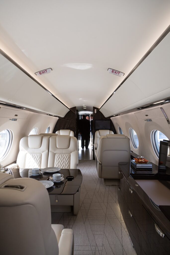 Cabin of a Gulfstream G600 with cream leather seats, wood tables and a row of oval windows