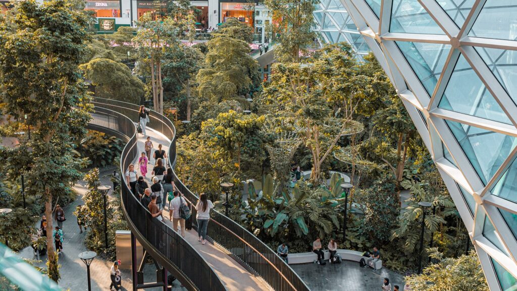 Passengers walking past tall trees and plants in The Orchard indoor garden at Doha Hamad International Airport