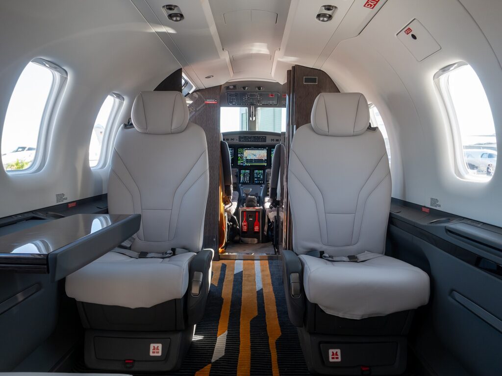 Pilatus PC-12 PRO cabin with two grey leather seats facing forward and the Garmin cockpit beyond