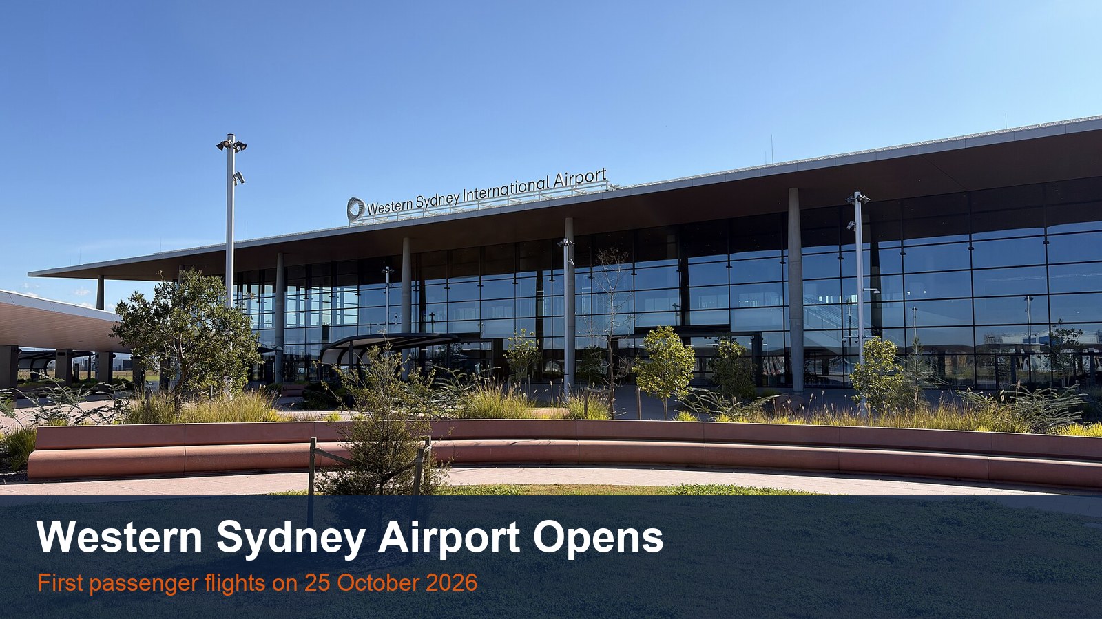 The glass front of the Western Sydney International Airport terminal under a blue sky, with the words Western Sydney Airport Opens